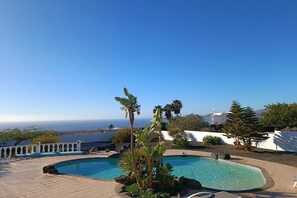 Una piscina con vista sull'oceano, circondata da piante tropicali e un recinto bianco.