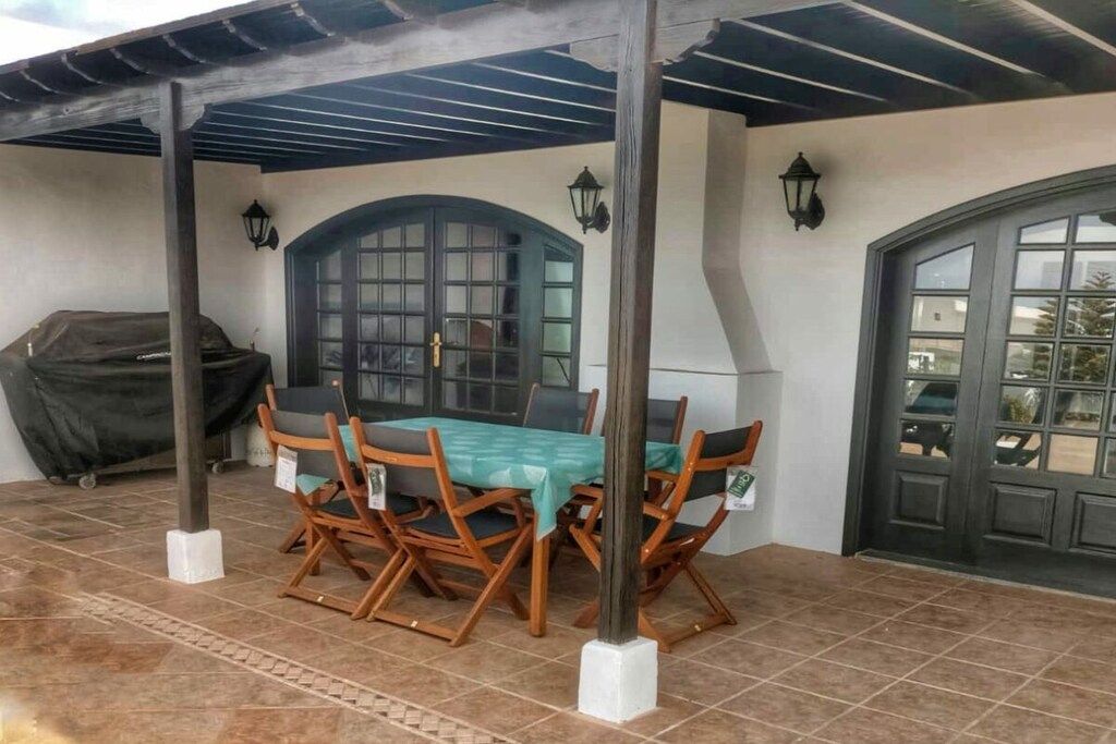 Un patio exterior con una mesa y sillas, una parrilla cubierta y una puerta con ventanal.