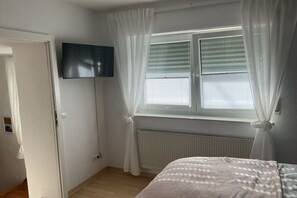 A bedroom with a bed, a window with blinds, a radiator, and a television mounted on the wall. - Holiday home with 2 bedrooms (Koblenz-Bassenheim)