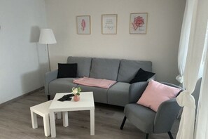 A modern living room with a grey sofa, a white coffee table, and a floor lamp. There are three framed artworks on the wall. - Holiday home with 2 bedrooms (Koblenz-Bassenheim)