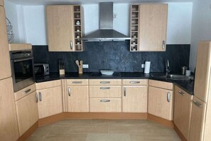 A kitchen with beige cabinets, a black countertop, a stainless steel range hood, and a tiled backsplash. - Holiday home with 2 bedrooms (Koblenz-Bassenheim)