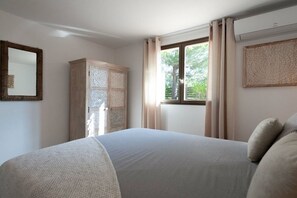A bedroom with a bed, a wardrobe, a window with curtains, and a wall-mounted mirror. - Casa Nina Authentic Corsica house (Porto Vecchio)