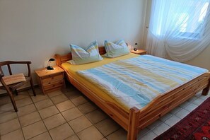 A bedroom with a wooden bed, two bedside tables, a chair, and a window with sheer curtains. - Holiday apartment in Ulmen with swimming pool (Ulmen)