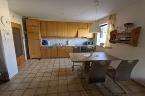 A compact kitchen with wooden cabinets, a dining table with chairs, a sink, and a window with a view. - Holiday apartment in Ulmen with swimming pool (Ulmen)