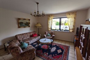A living room with a sofa, armchairs, a coffee table, a chandelier, a painting, and a window with curtains. - Holiday apartment in Ulmen with swimming pool (Ulmen)