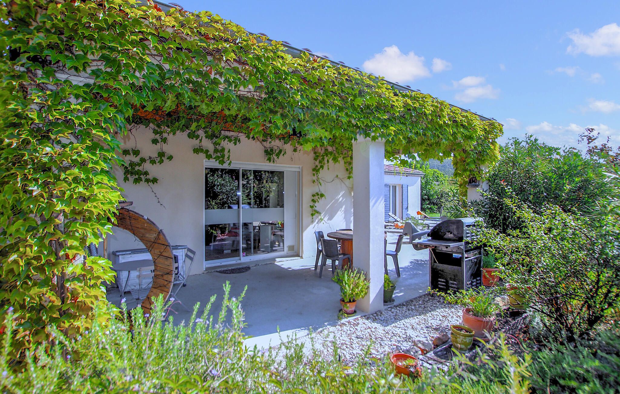 Eine überdachte Terrasse mit Grill, Sitzgelegenheiten im Freien und Blick auf das Haus.