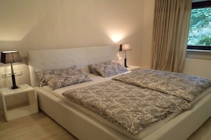 A bedroom with a large bed, two bedside lamps, and a window with curtains. - Holiday apartment with 2 bedrooms (Nieder-Olm)