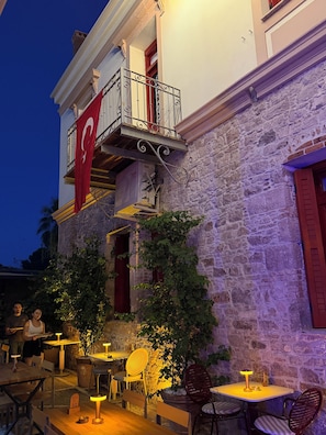 Un área de comedor al aire libre con mesas y sillas, un muro de piedra y una bandera.