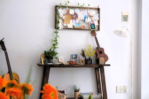 A room with a wooden music stand holding a guitar, a framed collage of notes, and a potted plant.