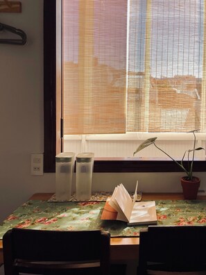 Ein Essbereich mit Tisch, Stühlen, einer Topfpflanze und einem Fenster mit Jalousien.