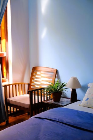 Una stanza con un letto, una sedia, un tavolo con una lampada e una pianta in vaso.