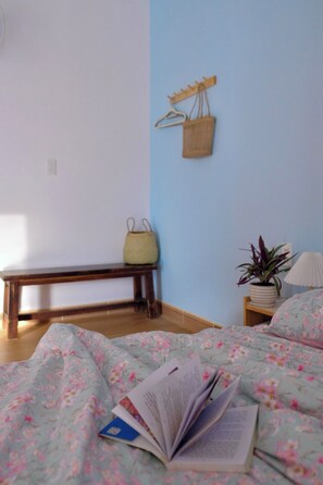 Ein Schlafzimmer mit einem Bett, einer Bank, einer hängenden Ampel, einem Blumentopf und einem Nachttisch mit Lampe.