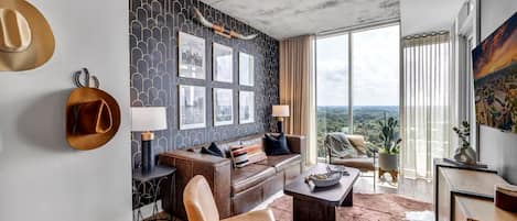 Una sala de estar moderna con un sofá de cuero, una mesa de centro y vistas de la ciudad a través de amplios ventanales.