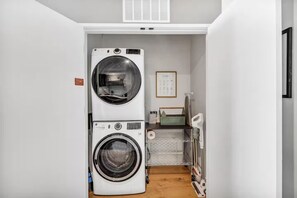 A laundry room with two stacked washing machines, a drying rack, and a small shelf with cleaning supplies. - Howdy, friends! Welcome to The Ranch on Rainey, where western charm meets urban chic! (Austin)