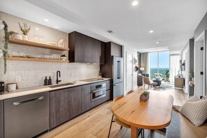 A modern kitchen with a wooden dining table, built-in appliances, and a view to the living area. - Howdy, friends! Welcome to The Ranch on Rainey, where western charm meets urban chic! (Austin)