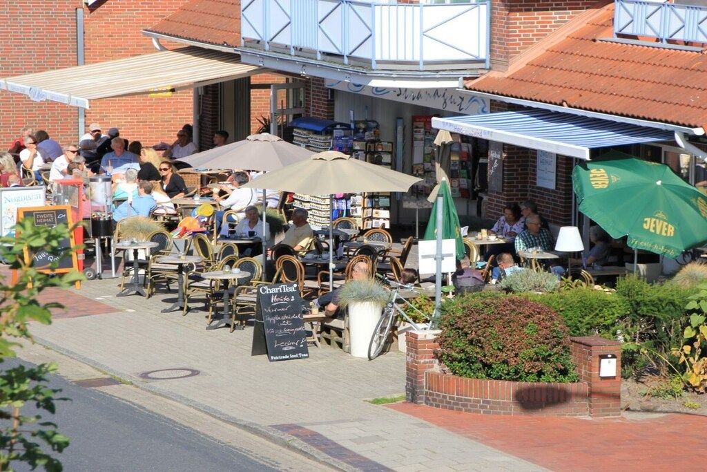 An outdoor café with tables and chairs, a signboard, and a green umbrella.