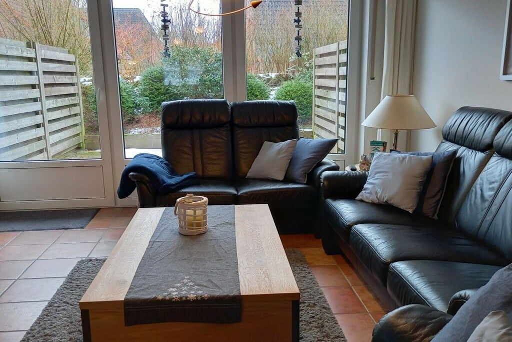 Un salon avec un canapé en cuir, une table basse en bois et une vue sur l’extérieur grâce à de grandes fenêtres.