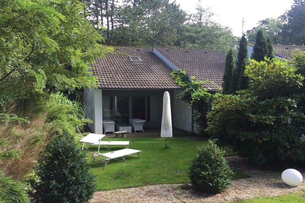 Une maison avec un toit en tuiles, un patio couvert avec des meubles d’extérieur et un jardin bien entretenu.
