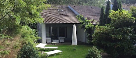 Una casa con techo de tejas, un porche cubierto con mobiliario exterior y un jardín bien cuidado.