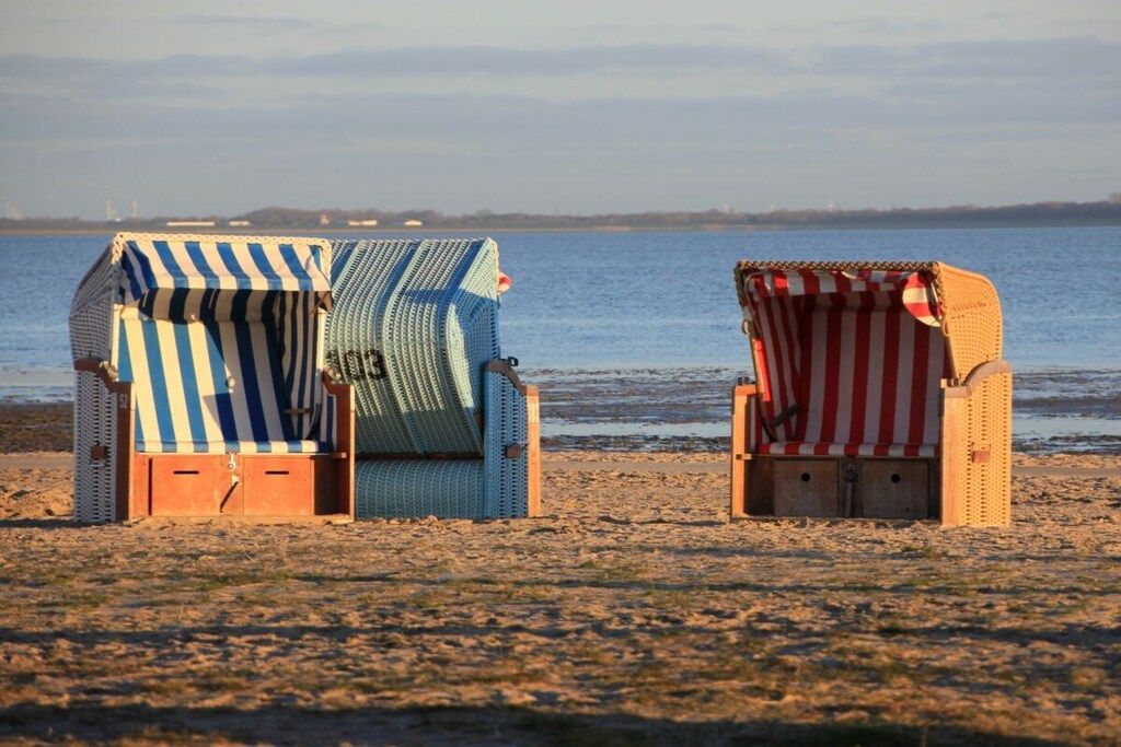 Two beach chairs with striped covers on a sandy beach with a body of water in the background.
