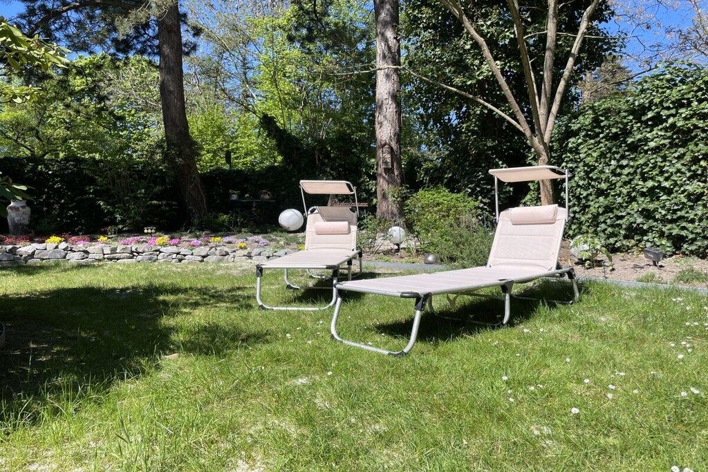Two lounge chairs in a garden setting with a stone wall and plants in the background.
