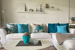 A white sofa with teal and white cushions, a teal vase, and decorative items on a white wall. - Holiday home with 1 bedroom (Varel - Dangast)