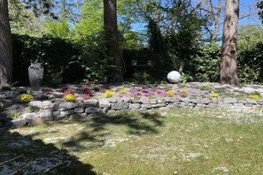 A garden with a stone wall, various colorful flowers, and trees. - Holiday home with 1 bedroom (Varel - Dangast)