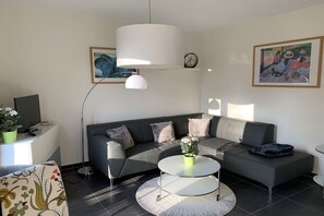 A modern living room with a grey sofa, a round coffee table, and a white pendant light. - Holiday apartment with 1 bedroom (Ostseebad Göhren)
