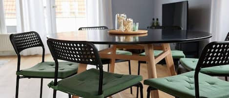 Un coin repas avec une table ronde, six chaises et un téléviseur en arrière-plan.