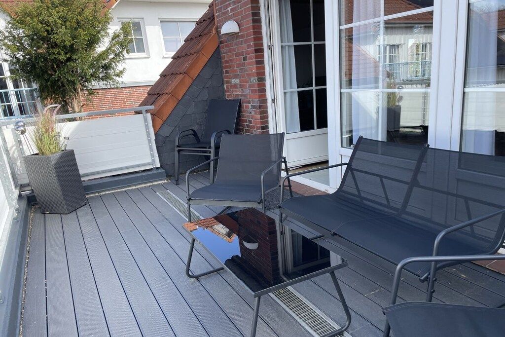 A covered outdoor seating area with chairs and a table, a brick wall, and a glass door leading to a balcony.