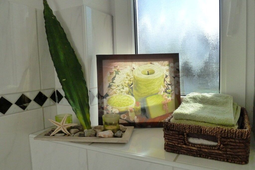 Ein Badezimmer mit Fenster, einem Bilderrahmen mit einer Kerze, einem Seestern und einem Korb mit Handtuch.