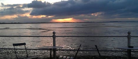 Une vue sur la mer avec une rambarde, un banc et une table.
