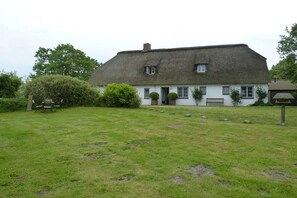 A traditional thatched-roof house with a well-maintained lawn and a bench. - Holiday home with 2 bedrooms (Osterhever)
