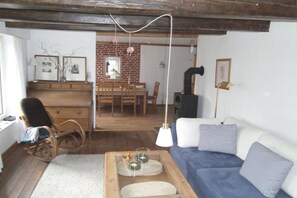 A cozy living room with a sofa, a rocking chair, a dining table, and a fireplace. - Holiday home with 2 bedrooms (Osterhever)