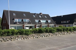 Ein zweistöckiges Haus mit geneigtem Dach, zahlreichen Fenstern und einer Steinmauer im Vordergrund.