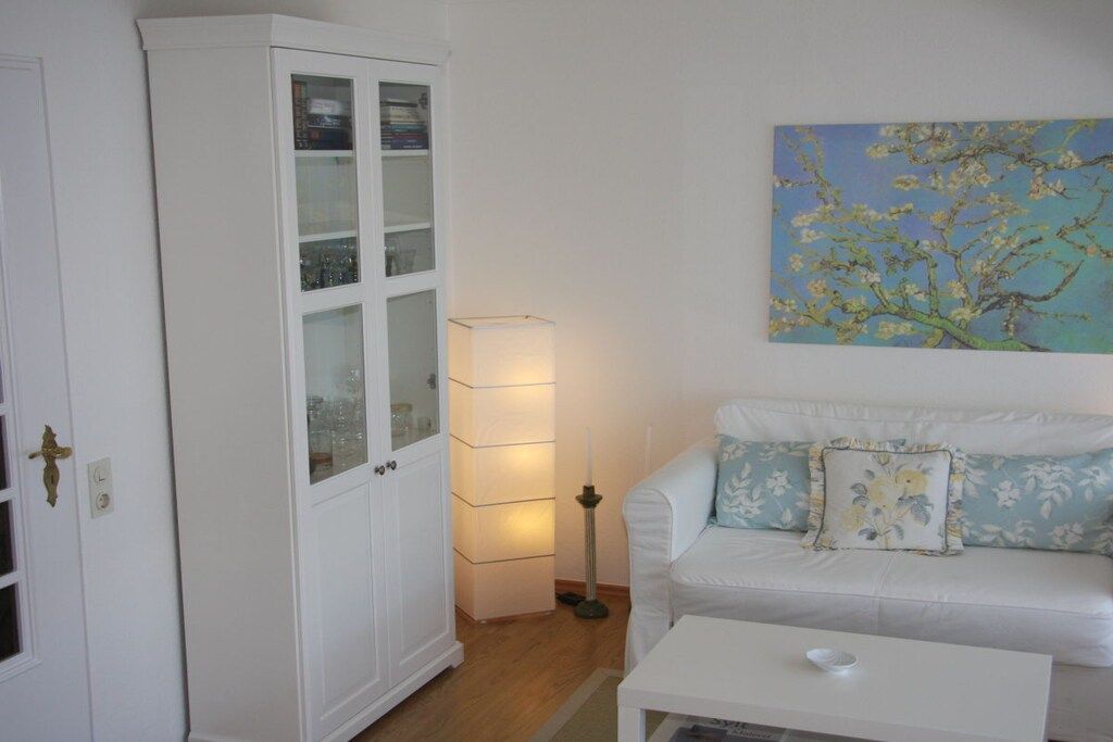 A room with a white cabinet, a white sofa with floral cushions, and a painting of a tree on the wall.