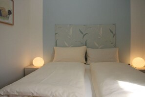 Ein Doppelbett mit zwei Nachttischlampen, ein Blattmuster an der Kopfteil und ein gerahmtes Bild an der Wand.
