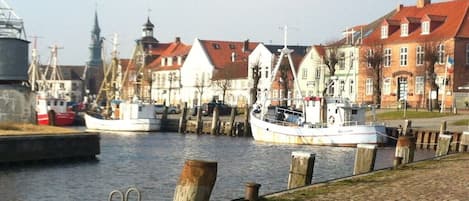 Een waterkant met aangemeerde boten, een geplaveid voetpad en traditionele gebouwen met rode daken.