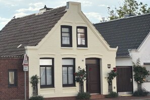 Ein zweistöckiges Haus mit einem steilen Dach, einer Haustür und einem kleinen Vorbereich mit Blumentöpfen.