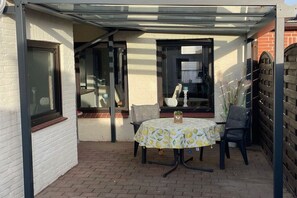 A patio with a table and chairs, a glass enclosure, and a brick floor. - Dimer, "little pearl" (Tönning)