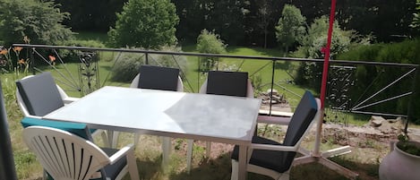 Une terrasse extérieure avec une table et des chaises, un parasol rouge et une vue sur un jardin et des arbres.