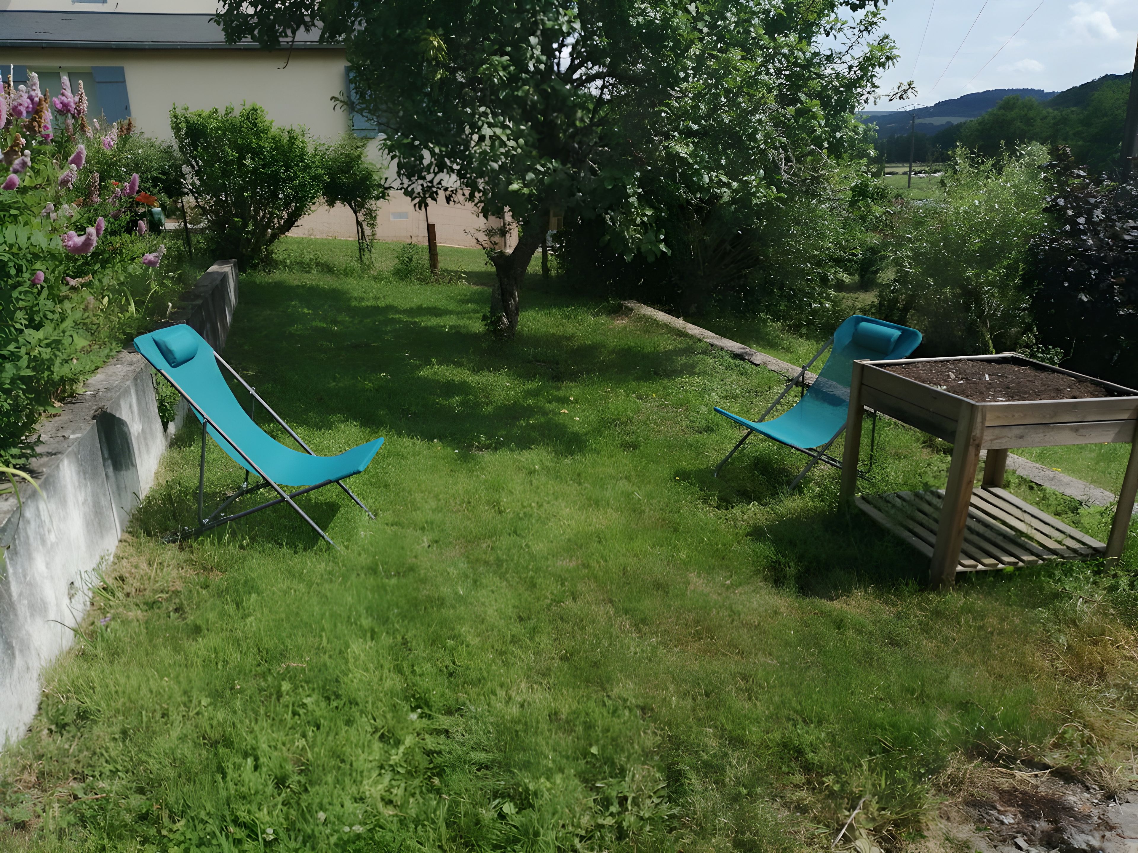 A grassy outdoor area with two blue chairs and a small table with a planter.