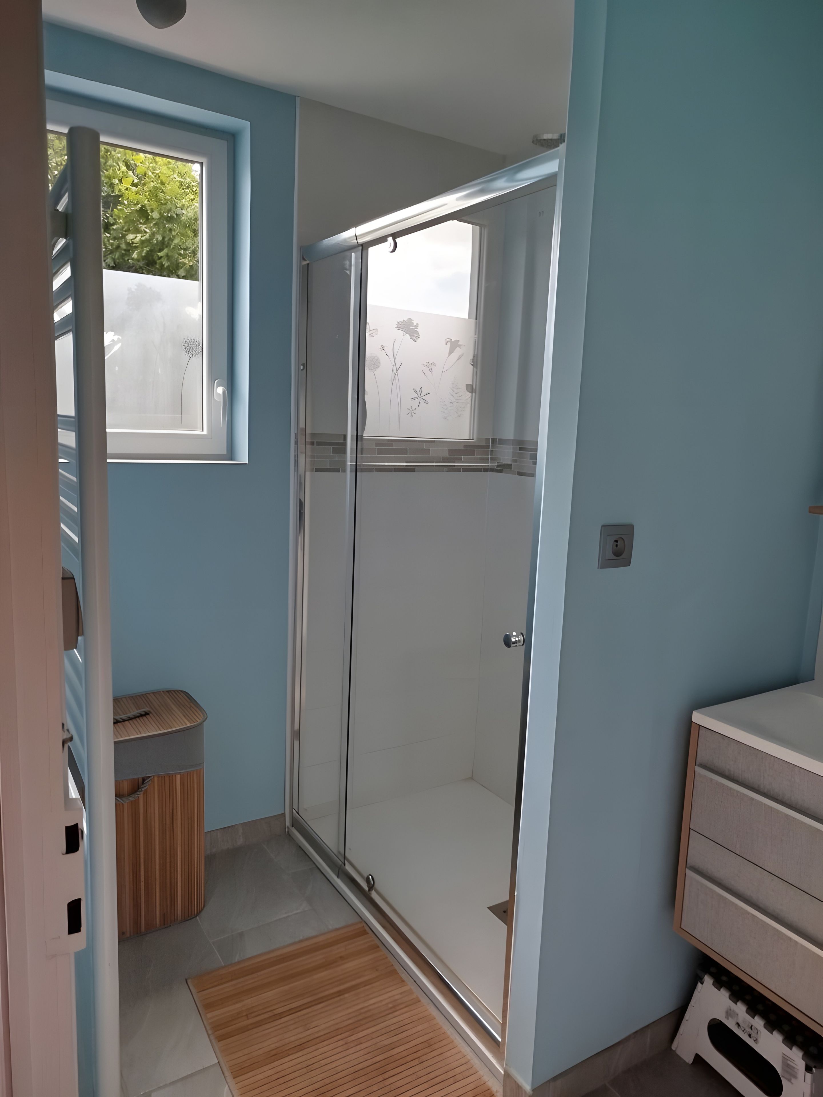 A bathroom with a shower, a window, and a wooden floor.