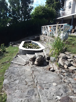 A stone pathway leading to a water feature with a white border, surrounded by rocks and plants. - Gîte Le Petit Buis: Mountain Views, Private Terraces & Wi-Fi (Chissey en Morvan)