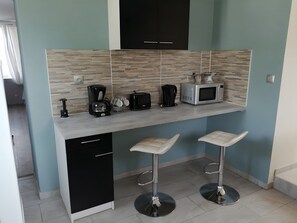 A compact kitchen with a built-in microwave, toaster, and coffee maker. There are two bar stools and a black dishwasher.