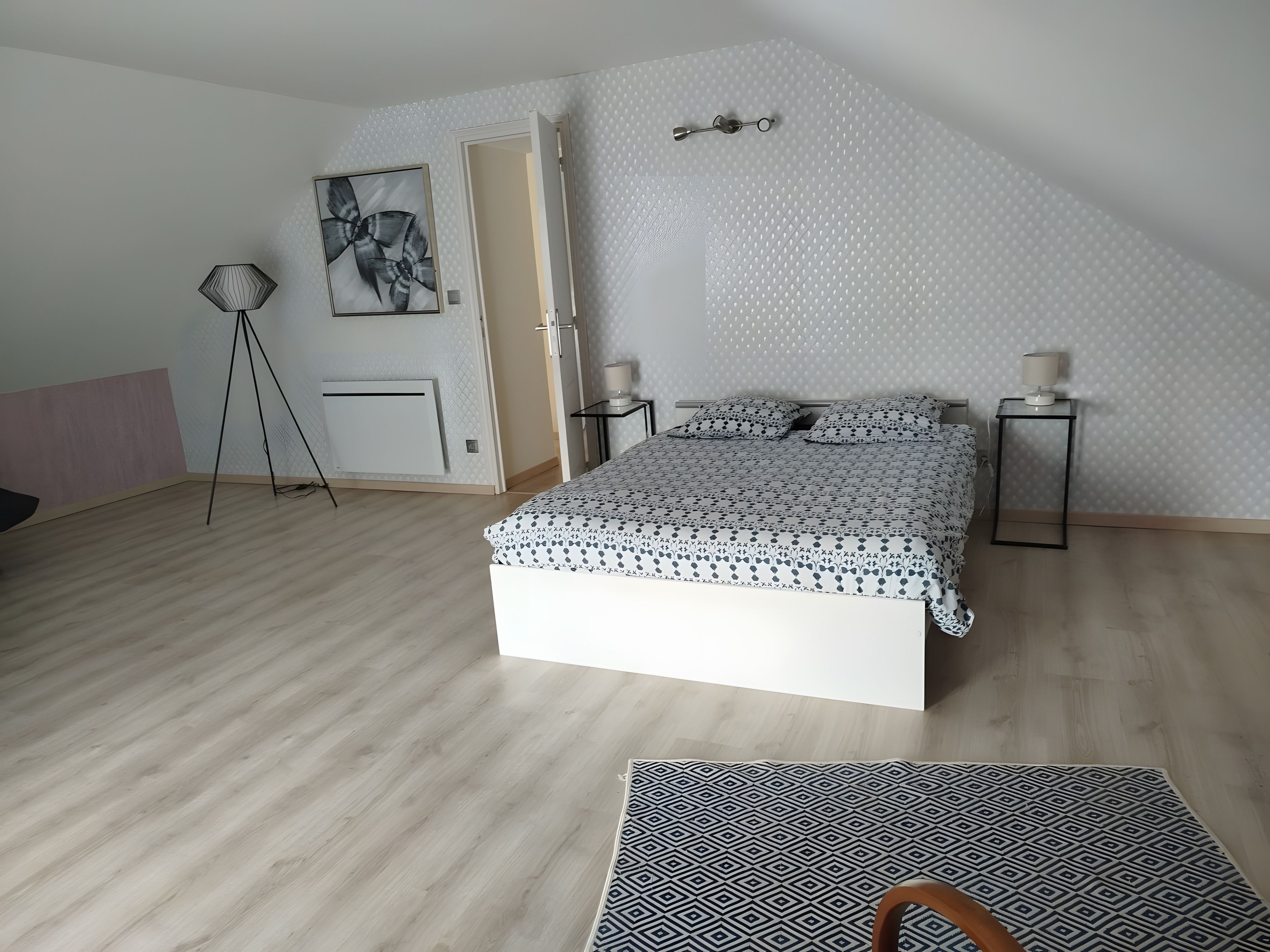 A bedroom with a bed, bedside tables, a lamp, a floor lamp, and a painting on the wall.