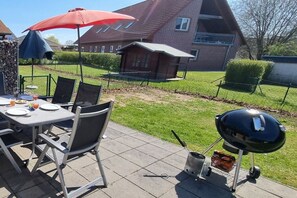 An outdoor patio with a table set for dining, a barbecue grill, and a house in the background. - Wismar cog starboard (Zierow)