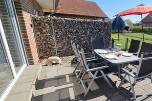An outdoor patio with a table and chairs, a stone wall, and a red umbrella. - Wismar cog starboard (Zierow)