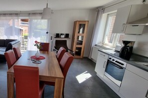 A modern kitchen with white cabinets, a built-in oven, and a dining area with a wooden table and red chairs. - Wismar cog starboard (Zierow)