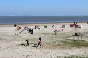 Ein Strand mit einem Spielplatz, Bänken und freiem Blick auf das Meer.